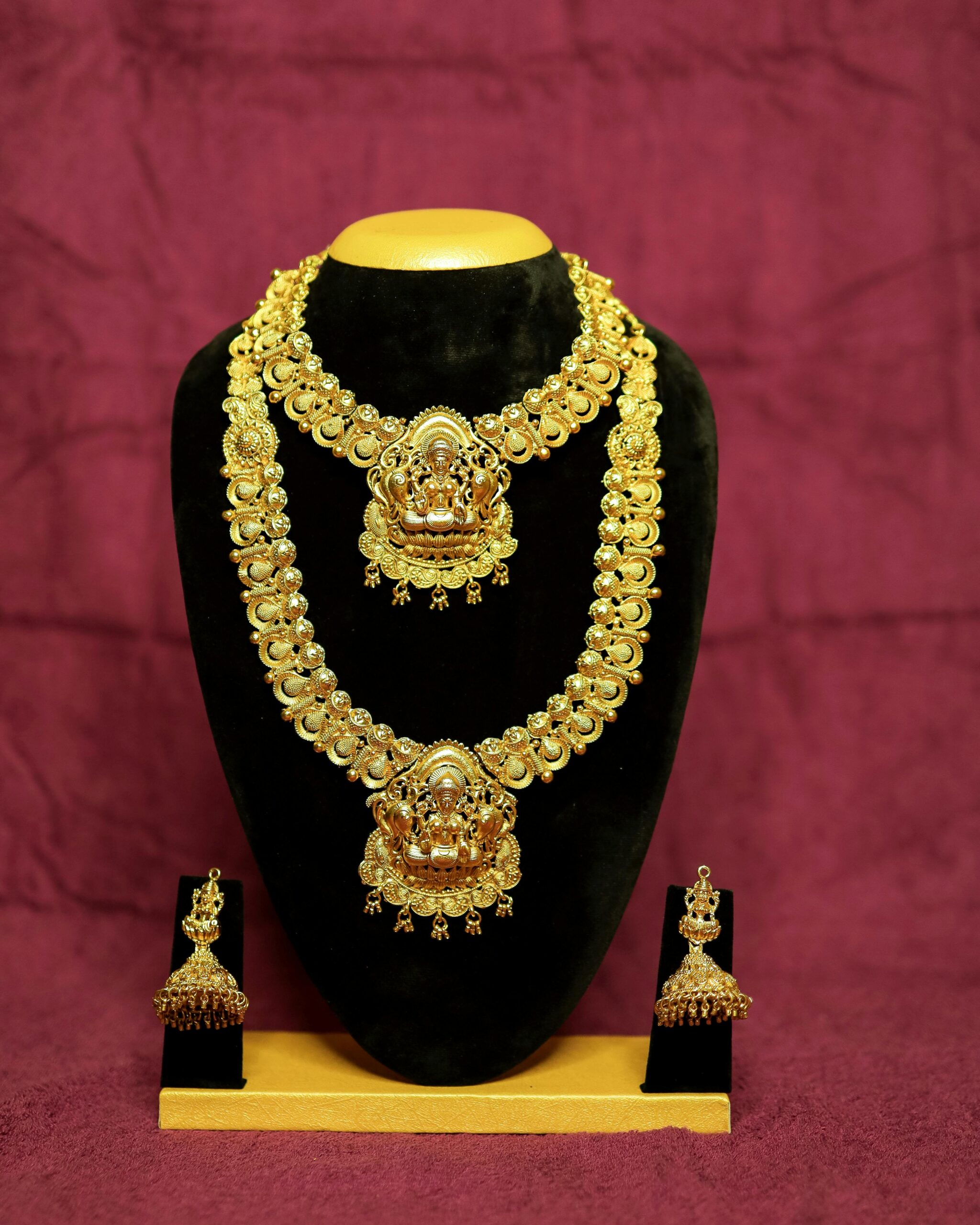 Intricate gold necklace and earrings displayed on black velvet with rich backdrop.