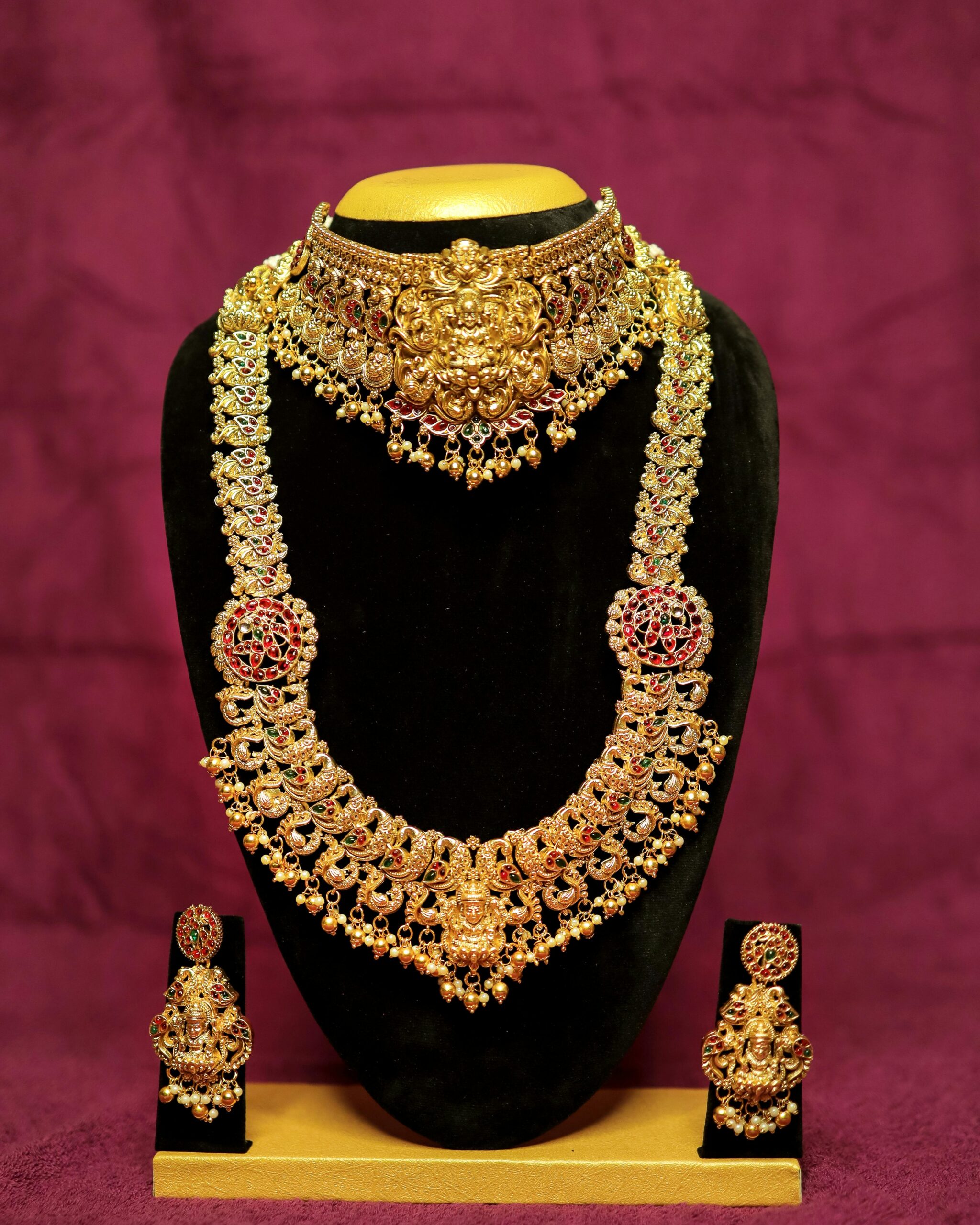 Elegant gold bridal jewelry set featuring necklace and earrings on a velvet stand.