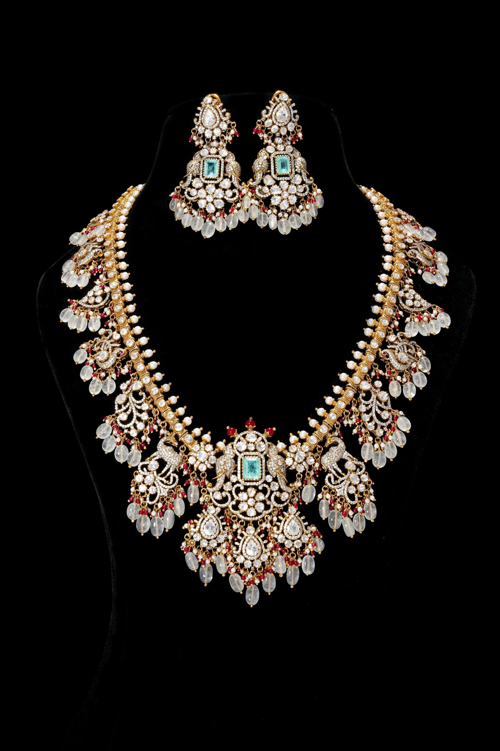 Luxurious ornate necklace and earring set with gemstones against black background.